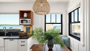 A kitchen with a view of the sea, a wooden table, and a hanging light fixture. - Historic Beach Cottage with Ocean View Deck - Steps to Beach (Dillon Beach)