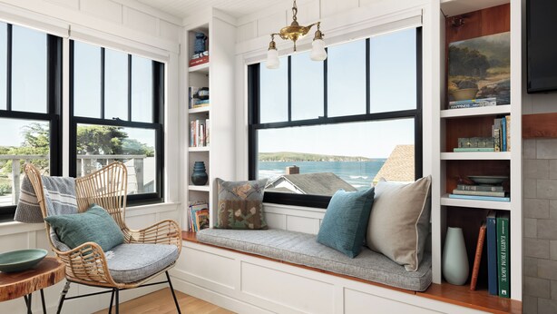 A cozy reading nook with a built-in bench, wicker chairs, and a bookshelf filled with books and decorative items. - Historic Beach Cottage with Ocean View Deck - Steps to Beach (Dillon Beach)