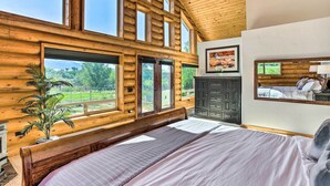 Une chambre située dans un chalet en rondins, avec un grand lit, un ventilateur de plafond et une vue sur l’extérieur.