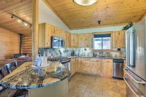 A kitchen with wooden cabinets, a granite countertop, stainless steel appliances, and a dining area with a leather couch.