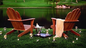 Twee houten Adirondack-stoelen gericht op een wateroppervlak, met een golfbaan op de achtergrond.