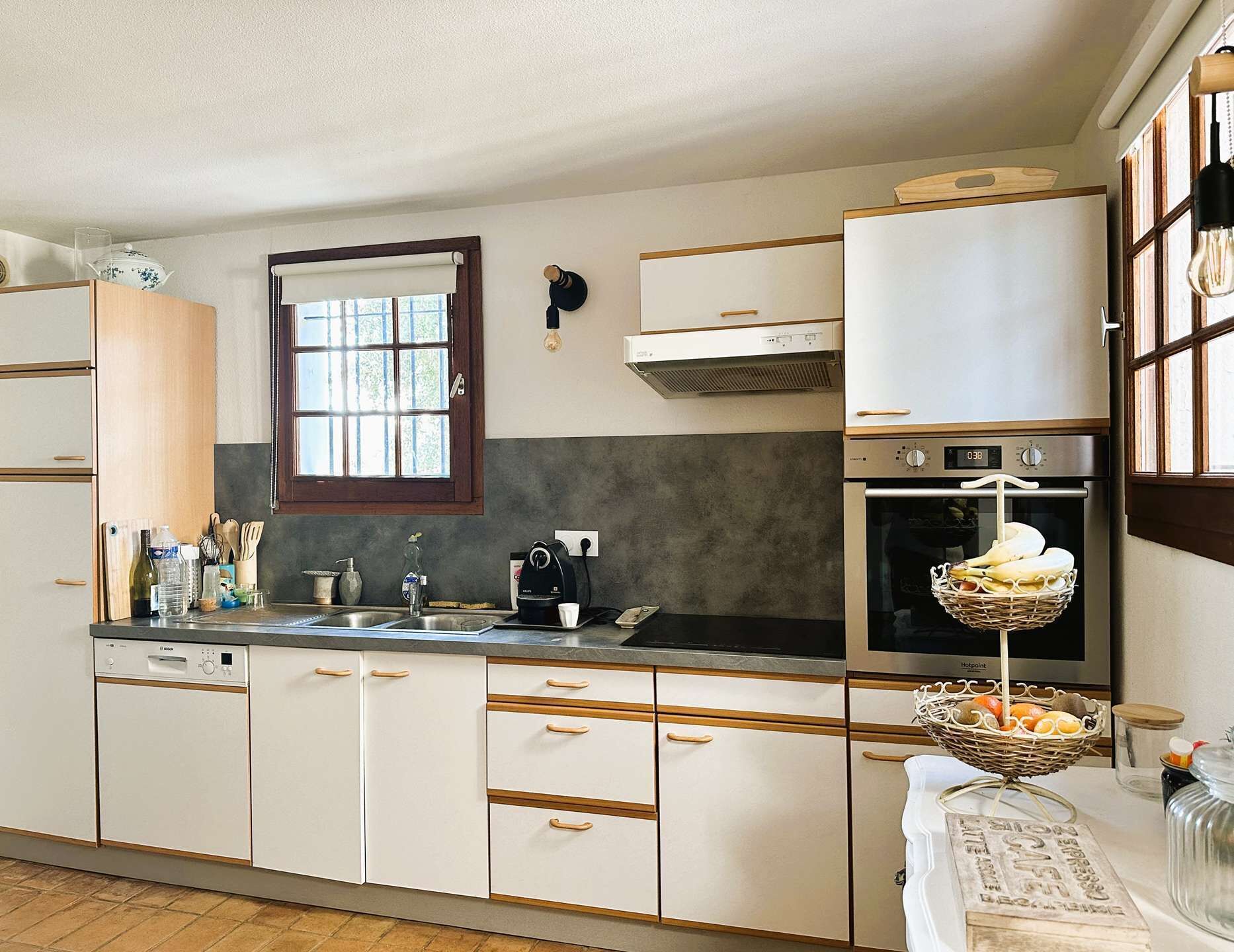 Una cocina con armarios blancos, una ventana, horno empotrado y una cesta de pan en la encimera.