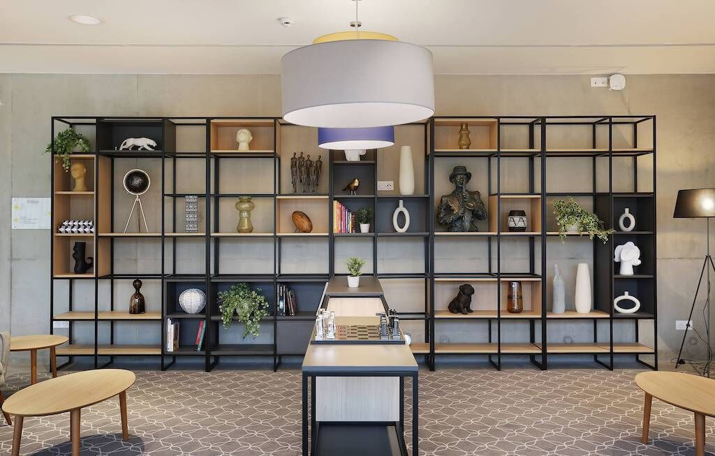 A modern interior with a central table, surrounded by black shelving units filled with various decorative items and plants.
