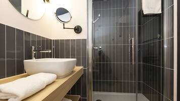 Une salle de bain moderne avec un grand lavabo blanc, un meuble-lavabo en bois, un miroir rond et une douche séparée par une paroi en verre.