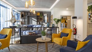 Een moderne zithoek met een bank, gele stoelen, een salontafel, en een keuken op de achtergrond.