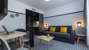 Una habitación de hotel moderna con un sofá, dos sillas, una mesita con una computadora portátil, una taza y un plato de fruta.