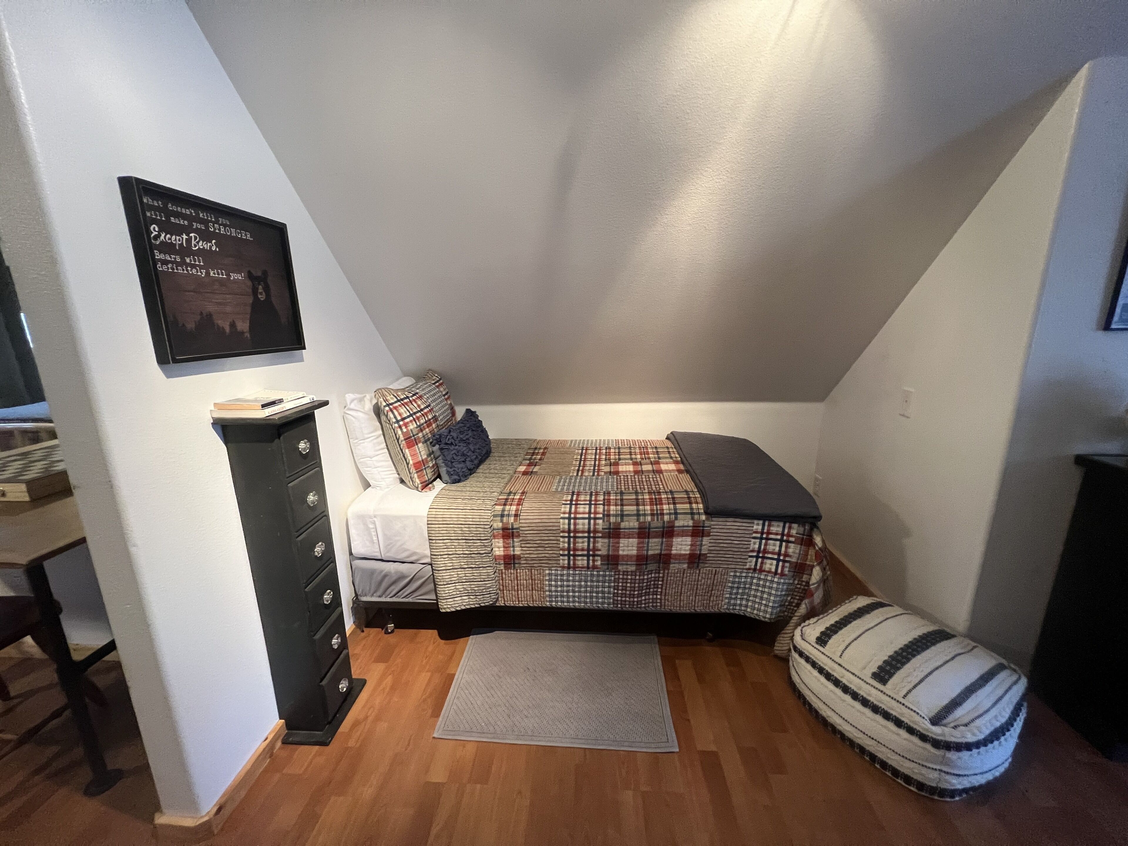 A small, cozy bedroom with a bed, a dresser, and a framed quote on the wall.