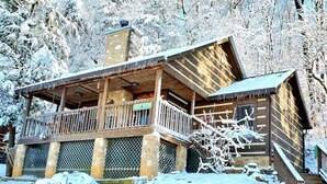 Una cabaña de madera con balcón, pilares de piedra y una entrada cubierta de nieve.