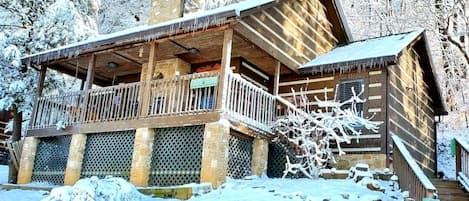 A wooden lodge with a balcony, stone pillars, and a snow-covered entrance.