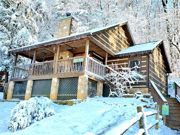 A wooden lodge with a balcony, stone pillars, and a snow-covered entrance.