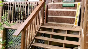 Una escalera de madera conduce a un porche con un letrero que dice 'Welcome', un cartel con la dirección '140 Smoky Mountain Way' y una pared rústica con detalles decorativos.