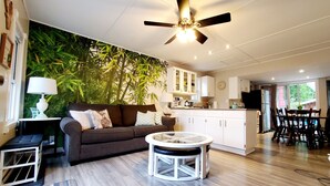 A modern living room with a brown sofa, a glass coffee table, and a ceiling fan. - Summer Beach Family Cottage  🏖 2min→beach @ Bamboo Chalet ~ Lake Erie 🇨🇦 
 (Turkey Point)