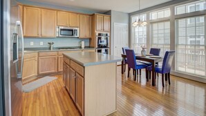 A modern kitchen with wooden cabinets, a central island, and a dining area with blue chairs.