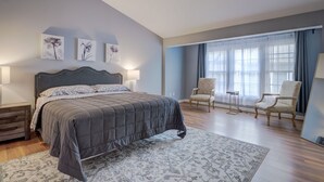 A bedroom with a large bed, two chairs, a small table, and a window with curtains.