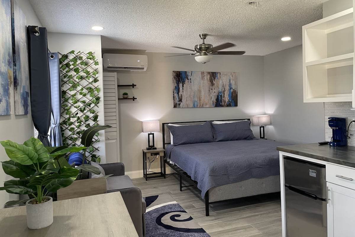 A modern bedroom with a bed, bedside lamps, a ceiling fan, and a built-in dishwasher.