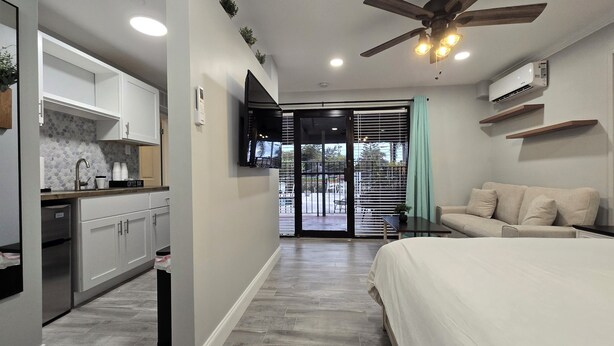 A modern bedroom with a bed, a ceiling fan, a TV, and a sliding glass door leading to a balcony. - Sunny Palms Inn (Lake Worth)