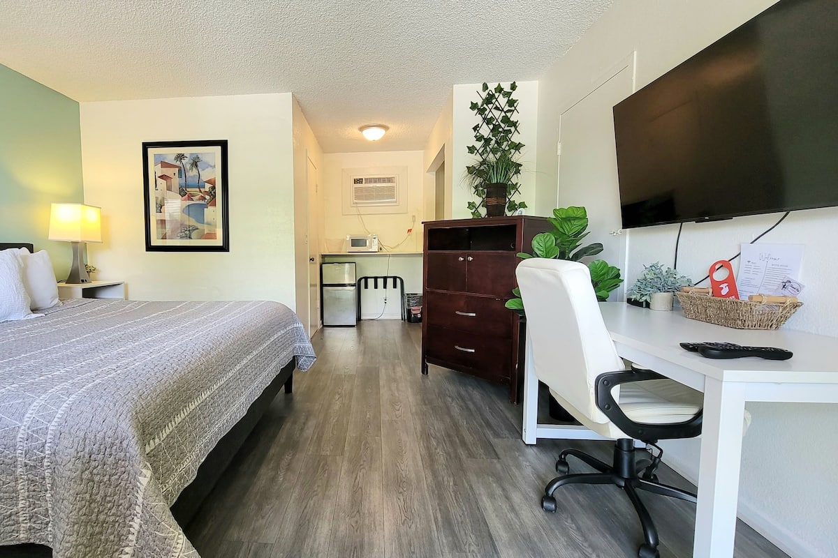 A hotel room with a bed, desk, chair, dresser, and a TV mounted on the wall.