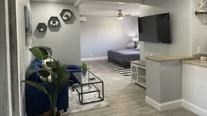 A modern living room with a blue sofa, a glass coffee table, and a large plant. - Sunny Palms Inn (Lake Worth)