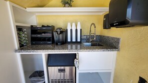 A compact kitchen with a granite countertop, a coffee maker, a kettle, and a coffee dispenser.