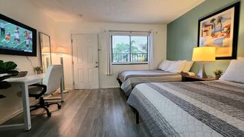 Quarto de hotel com duas camas, uma escrivaninha, televisão e janela com persianas.