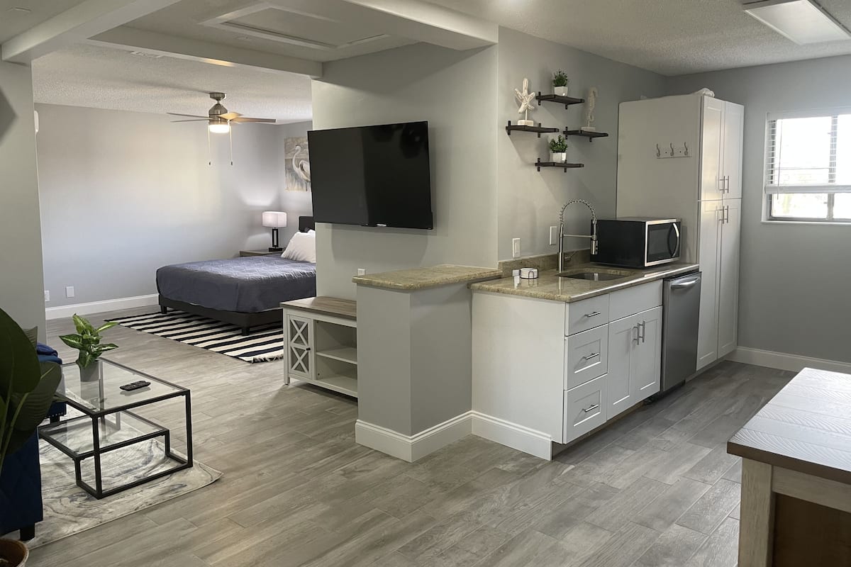 A compact living space with a kitchenette, a bed, a TV, and a ceiling fan.