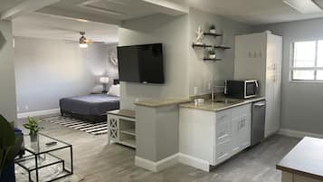 Un espacio habitable compacto con kitchenette, cama, televisor y ventilador de techo.