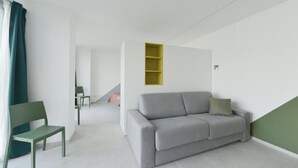 Een minimalistische woonkamer met een grijze bank, een groene fauteuil en een geel wandrek.