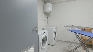 Een wasserij met twee wasmachines, een droogmachine, een luchtverwarmer aan het plafond en een opklaptafel.