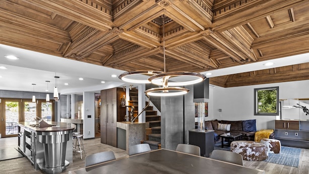 A spacious living area with a large dining table, a kitchen island, and a staircase leading to an upper level.