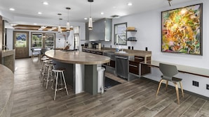 A modern kitchen with a central island, bar stools, stainless steel appliances, and a large abstract painting.