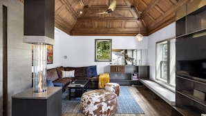 A modern living room with a wooden ceiling, a large TV, a sofa, ottomans, and a coffee table.