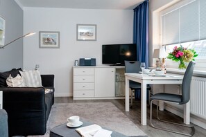 Ein modernes Hotelzimmer mit Wohnbereich, einem Esstisch, einem Fernseher und einem Fenster mit Vorhängen.