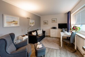 Ein modernes Wohnzimmer mit grauem Sofa, einem kleinen Tisch, einem Fernseher und Kunstwerken an den Wänden.