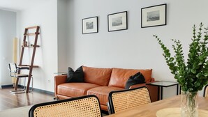A modern living room with a brown leather sofa, black cushions, a wooden coffee table, wicker chairs, and a glass vase with green plants. - Sun Terrace Penthouse Living4malaga (Málaga)