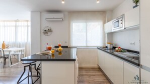 A modern kitchen with a central island, white cabinetry, and a microwave. There is a dining area with a table and chairs to the left.