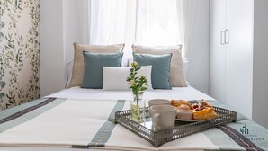 A neatly made bed with a tray of pastries and two mugs, a vase with flowers, and a floral wallpaper.