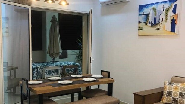 Un coin repas avec une table dressée pour quatre personnes, un banc et un canapé. Il y a un tableau au mur et un luminaire au plafond.