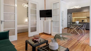 A modern living room with a sofa, a coffee table, and a TV. There is a kitchen area with a dining table and chairs. - 3Bdr Modern Design & Bright Interiors in Plaka (Athens)