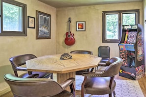 A room with a wooden table, leather chairs, a guitar, framed pictures, and a pinball machine. - Cozy Florence Cabin, Proximity to Keyes Peak! (Florence)