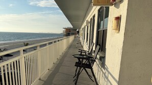 A balcony with a view of the beach, a white railing, and a table with chairs.