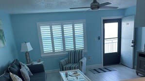 A living room with a dark blue sofa, a striped armchair, a white coffee table, and a ceiling fan.