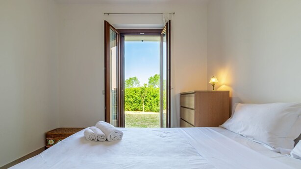 A bedroom with a bed, a nightstand, a lamp, and a view of greenery outside. - Nice apartment for 4 people with WIFI, TV and patio, close to Porto Recanati (Loreto)