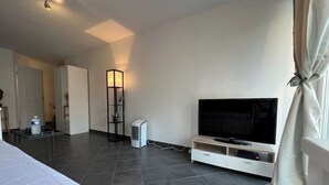 A hotel room with a bed, a TV on a stand, a heater, and a water dispenser. - Beau Studio Nice - Riquier (Nice)