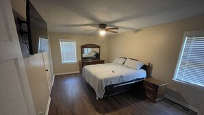 A bedroom with a bed, a ceiling fan, a dresser, and a window with blinds.