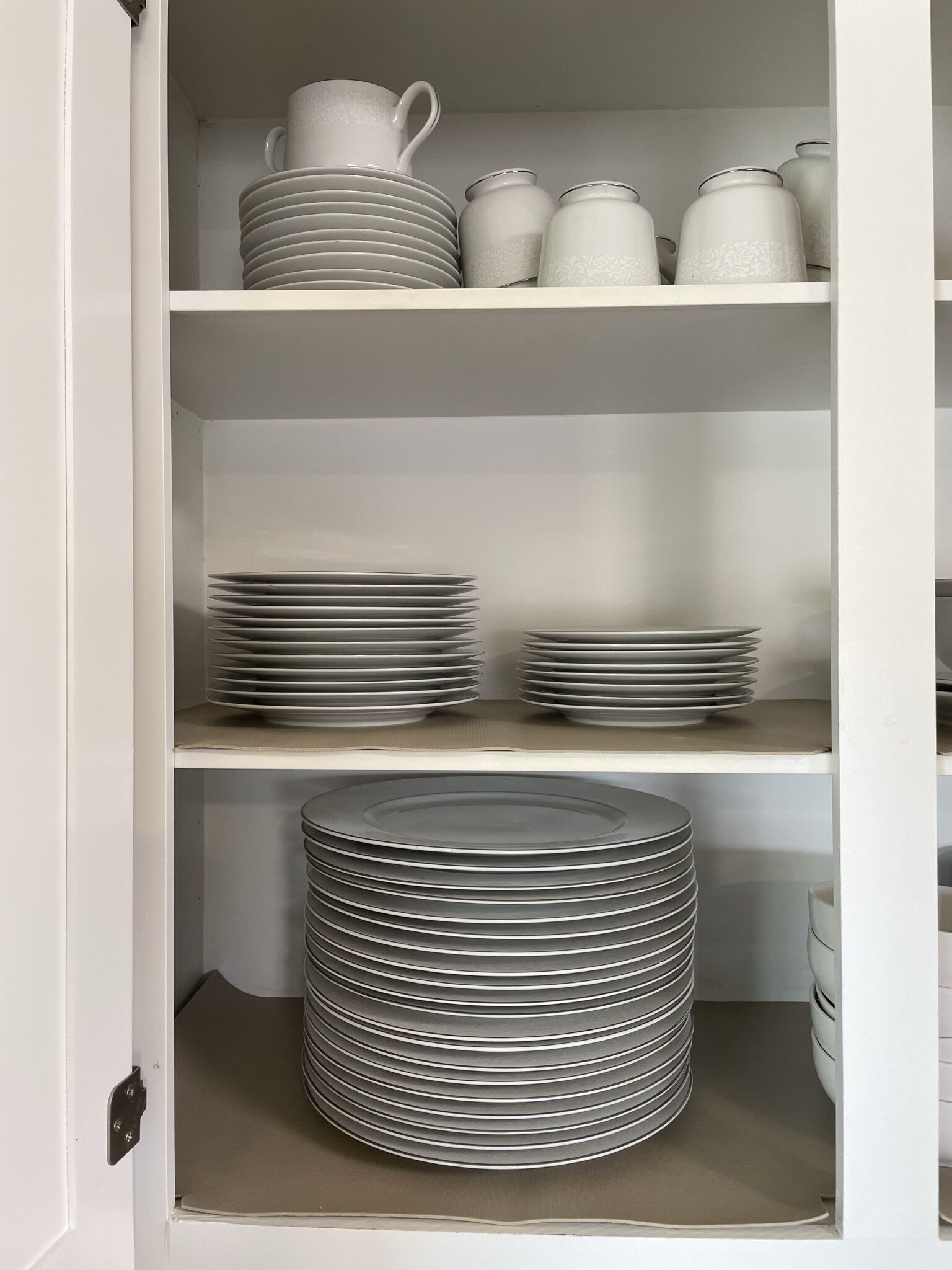 A white interior with shelves holding stacked plates, a large stack of plates, and white ceramic containers.