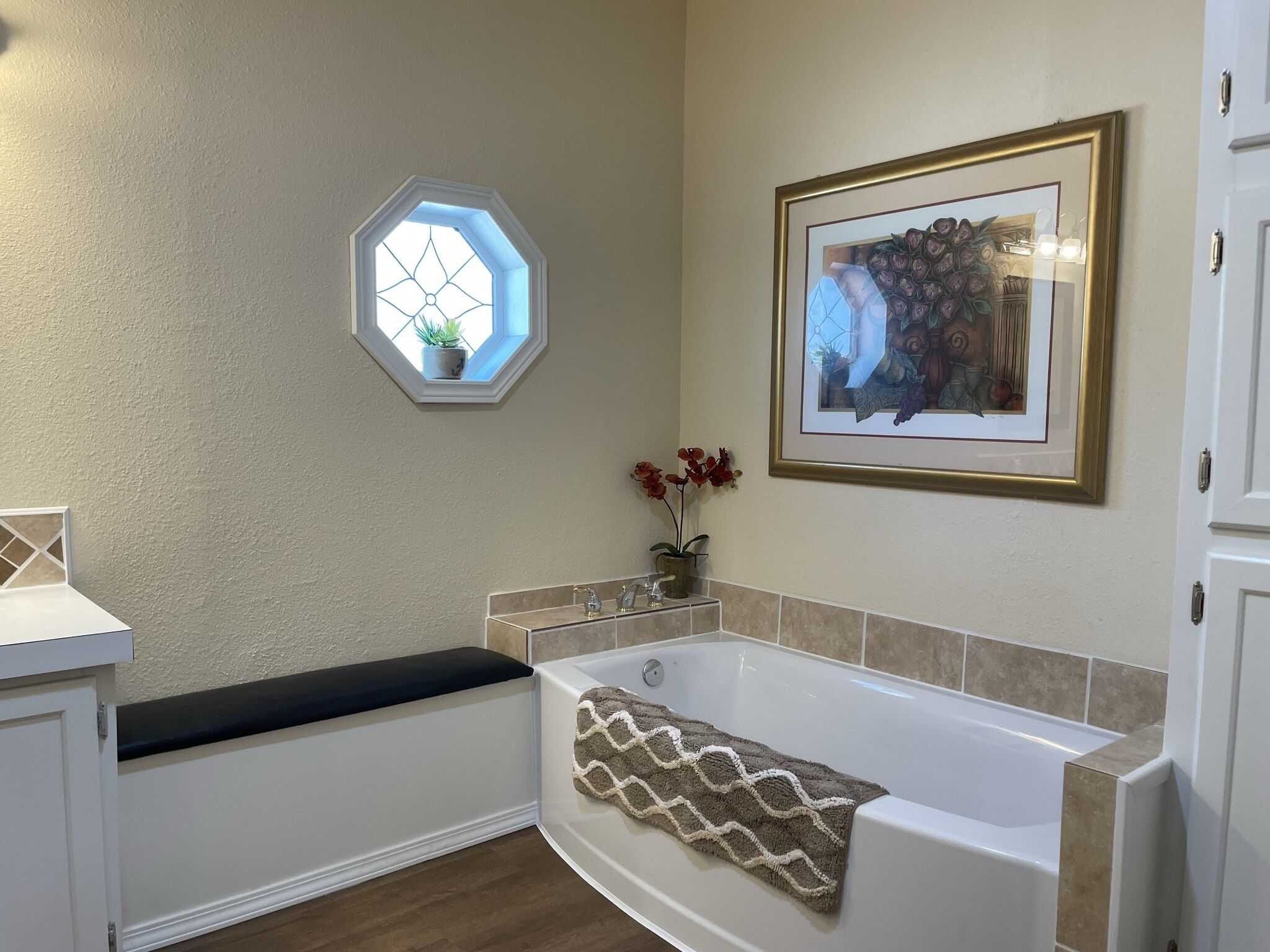 A bathroom with a bathtub, a window, a framed picture, and a potted plant.