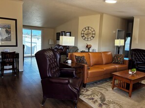 A living room with a brown leather sofa, a dark leather armchair, a wooden coffee table, and a large wall clock.