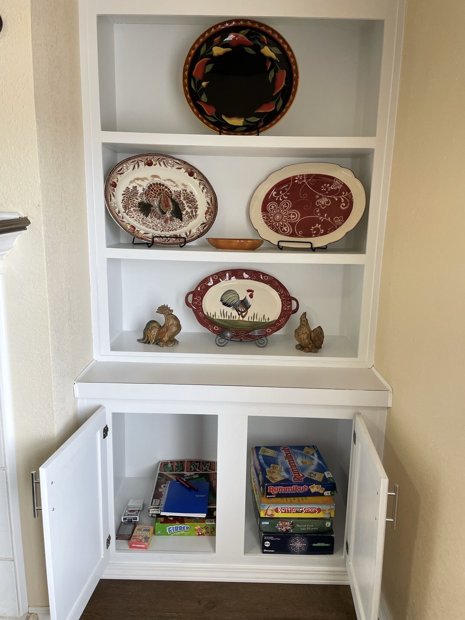 A white cabinet with shelves containing decorative plates, a bowl, and children's board games.
