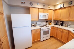 Une cuisine avec des meubles de rangement en bois, un réfrigérateur blanc, un four à micro-ondes, une cuisinière et un grille-pain.