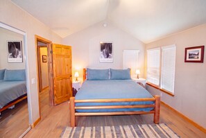 Une chambre à coucher avec un grand lit, une porte en bois, deux tables de chevet avec des lampes et une fenêtre avec des stores.